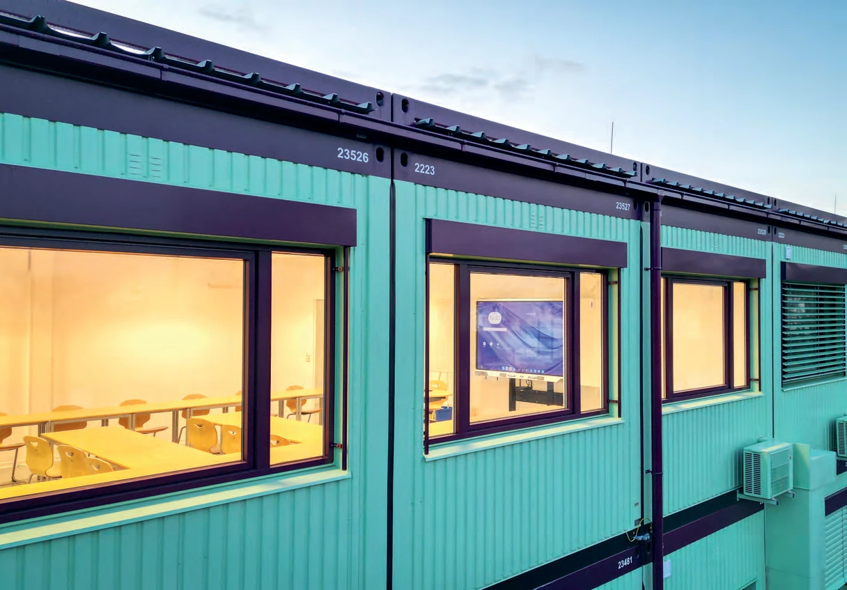 Fassade einer X-class Schulanlage mit großen, hell erleuchteten Klassenraumfenstern